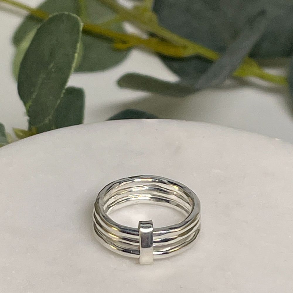 Silver chunky ring with three bands on a white surface with green leaves in the background