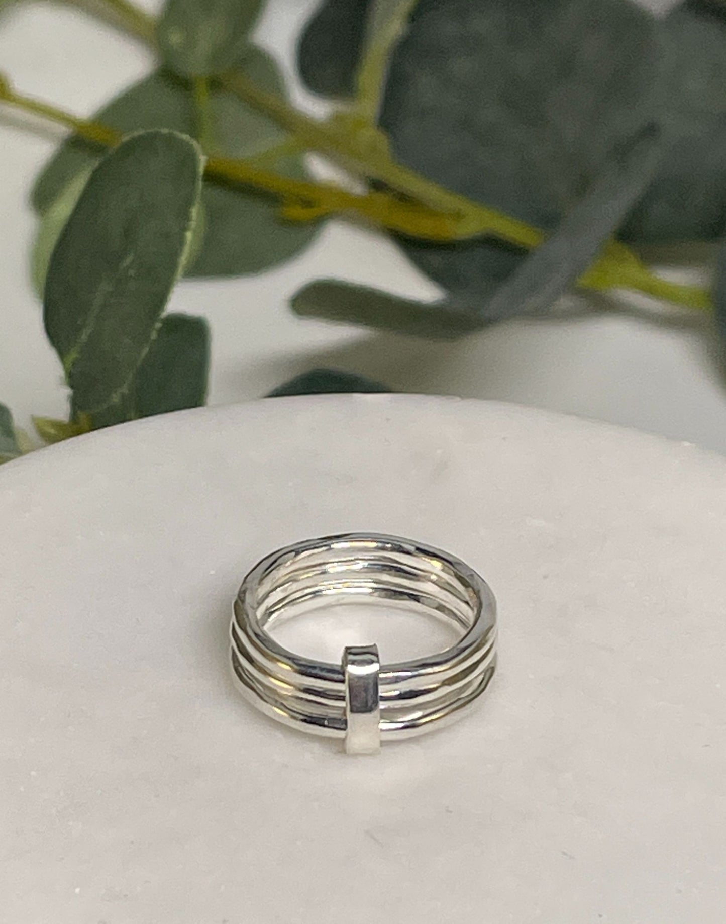 Silver chunky ring with three bands on a white surface with green leaves in the background