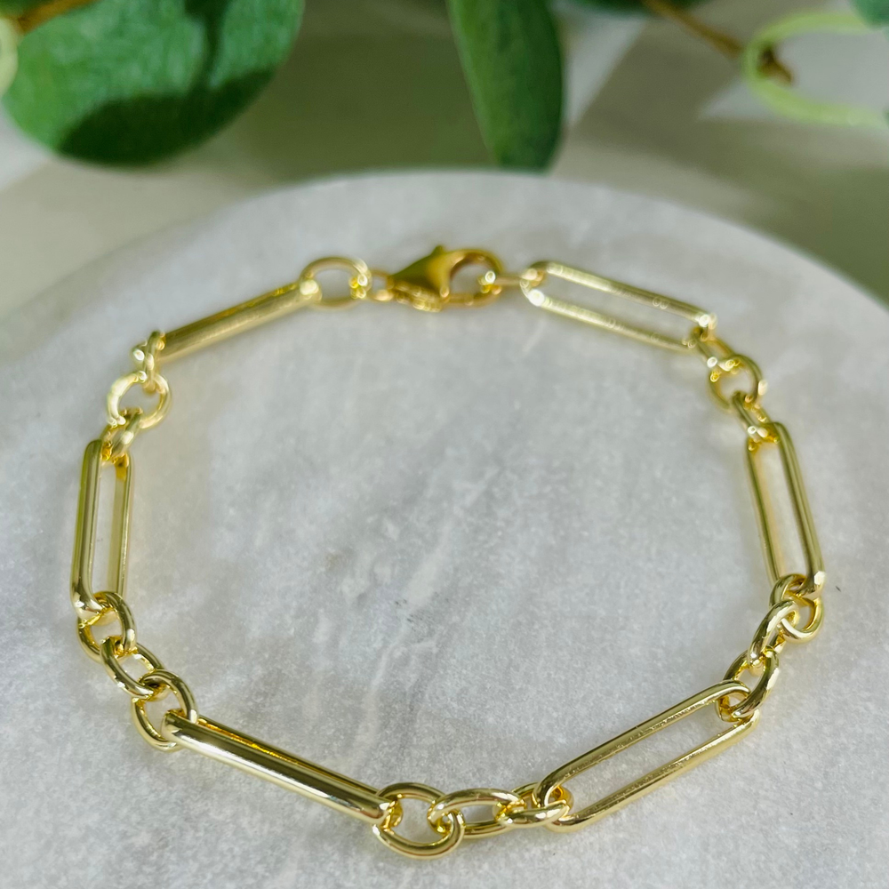 Gold bracelet on a white surface with green leaves in the background