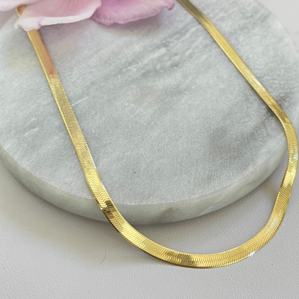 Gold herringbone necklace on a tile