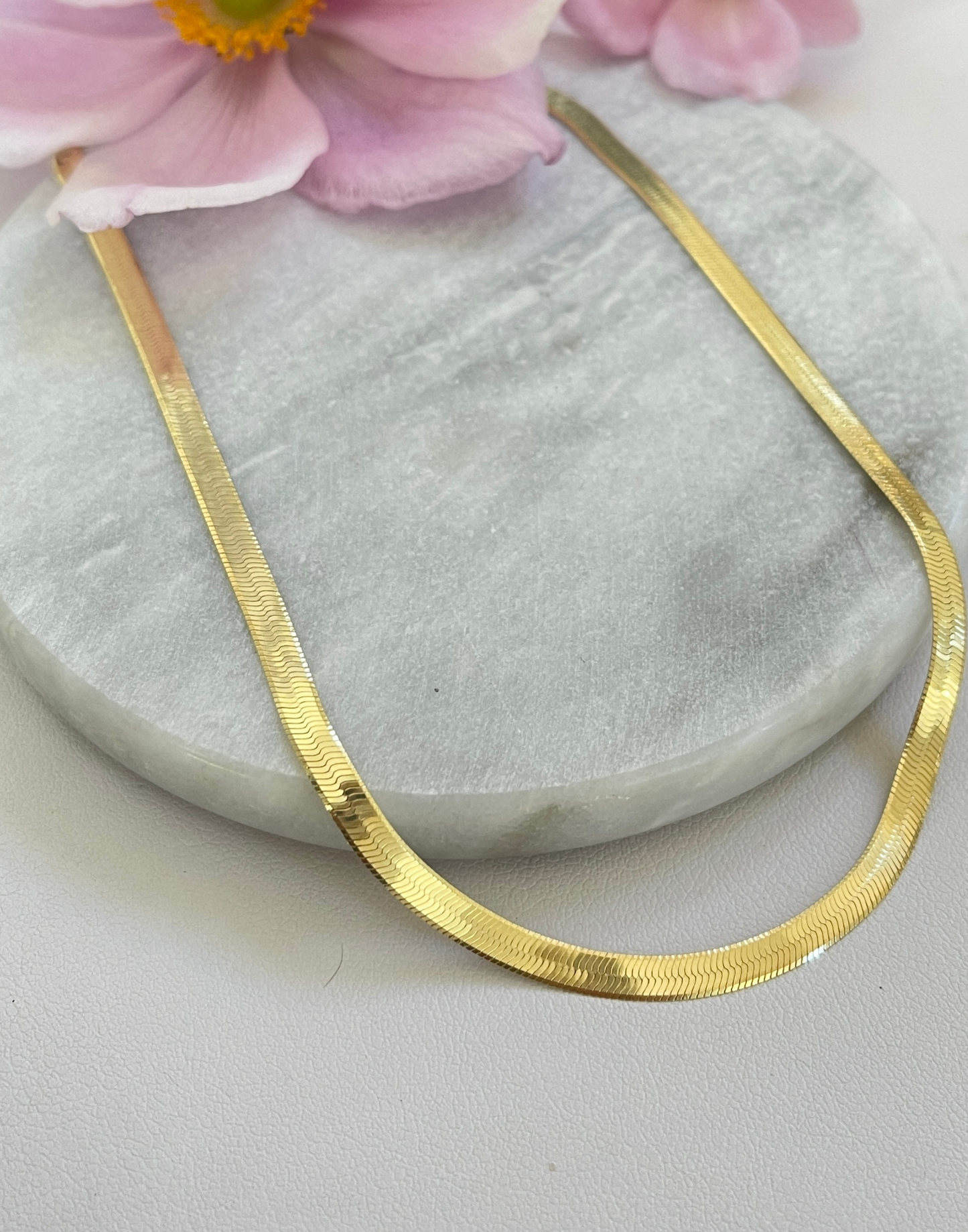 Gold herringbone necklace on a tile