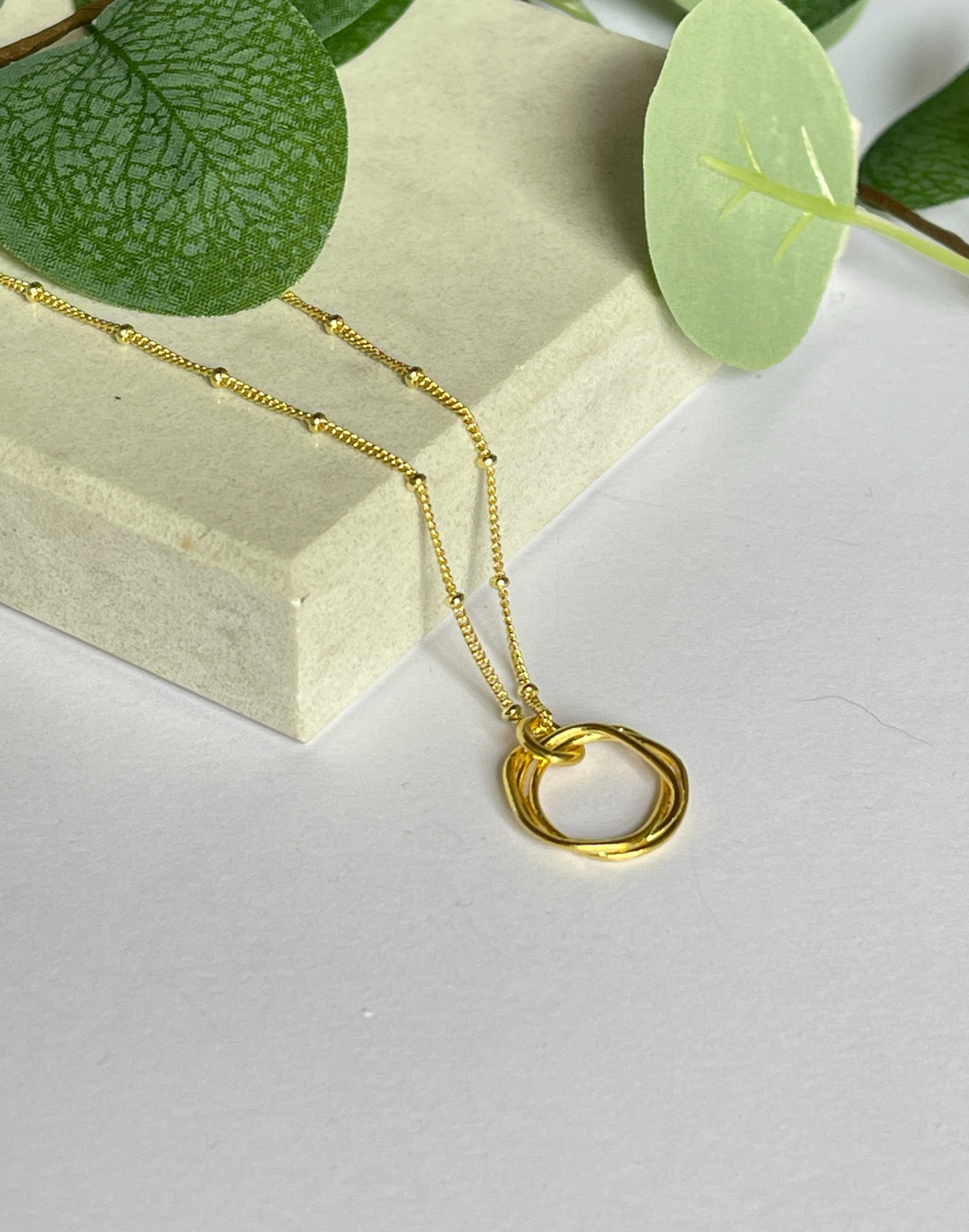 gold twisted circle necklace on tile