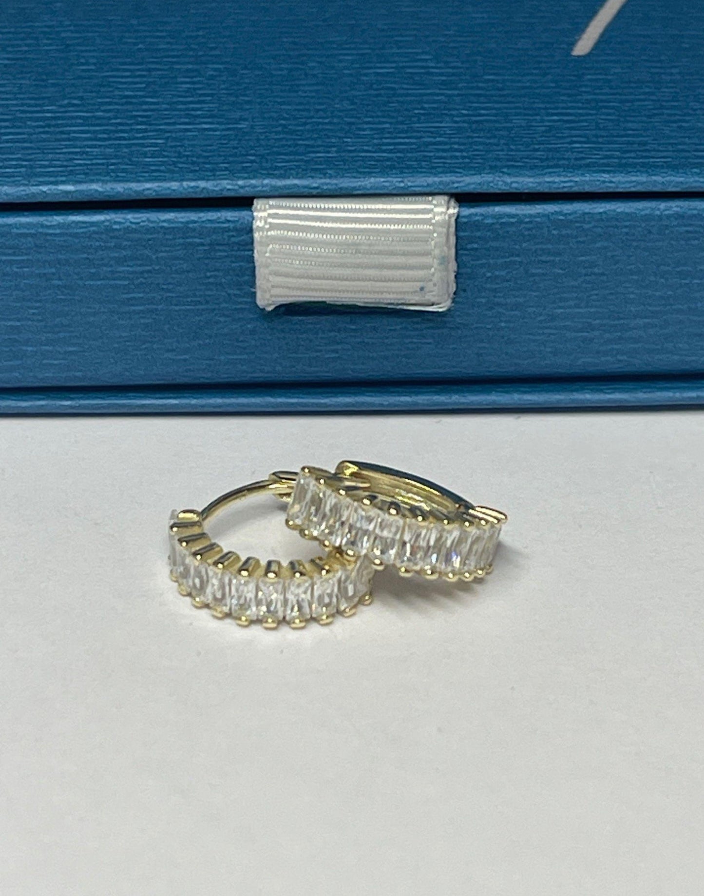 gold and crystal holiday huggie earrings on a tile next to a Flutterby gift box