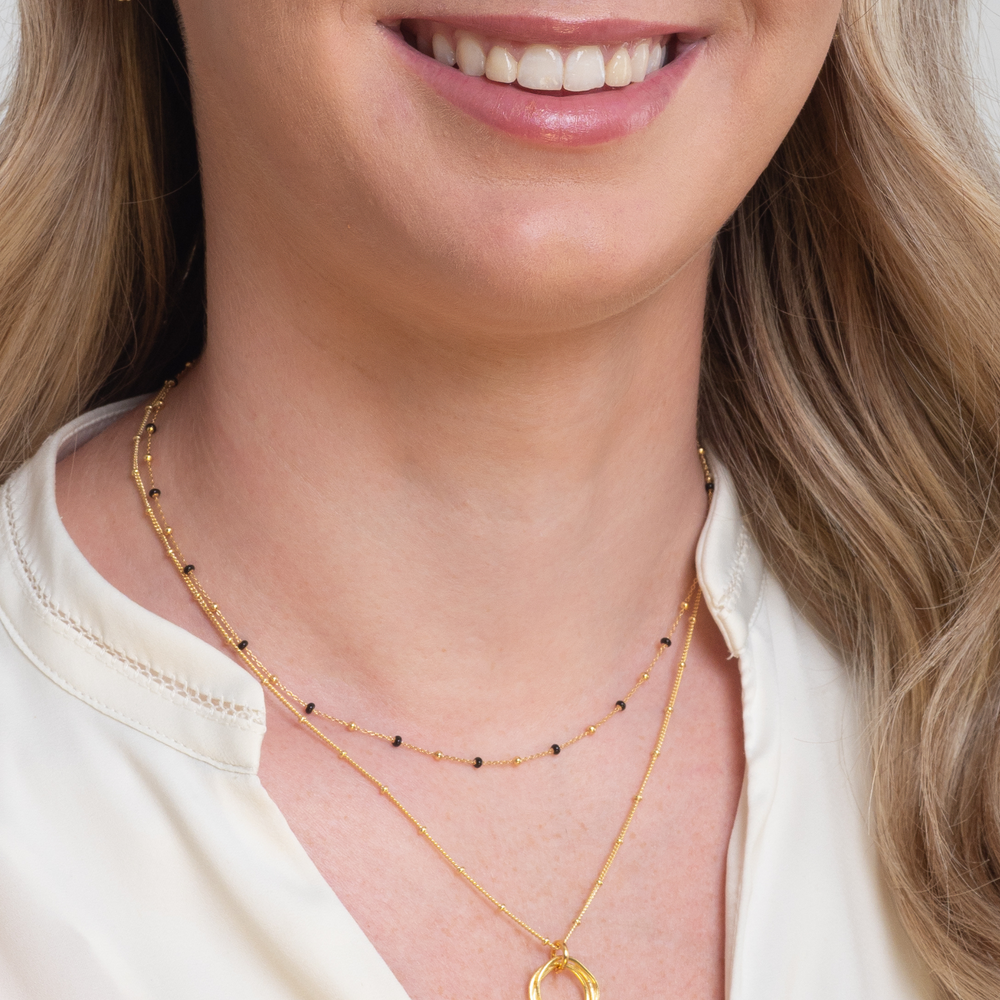 model wears gold black enamel necklace with gold twisted circle necklace