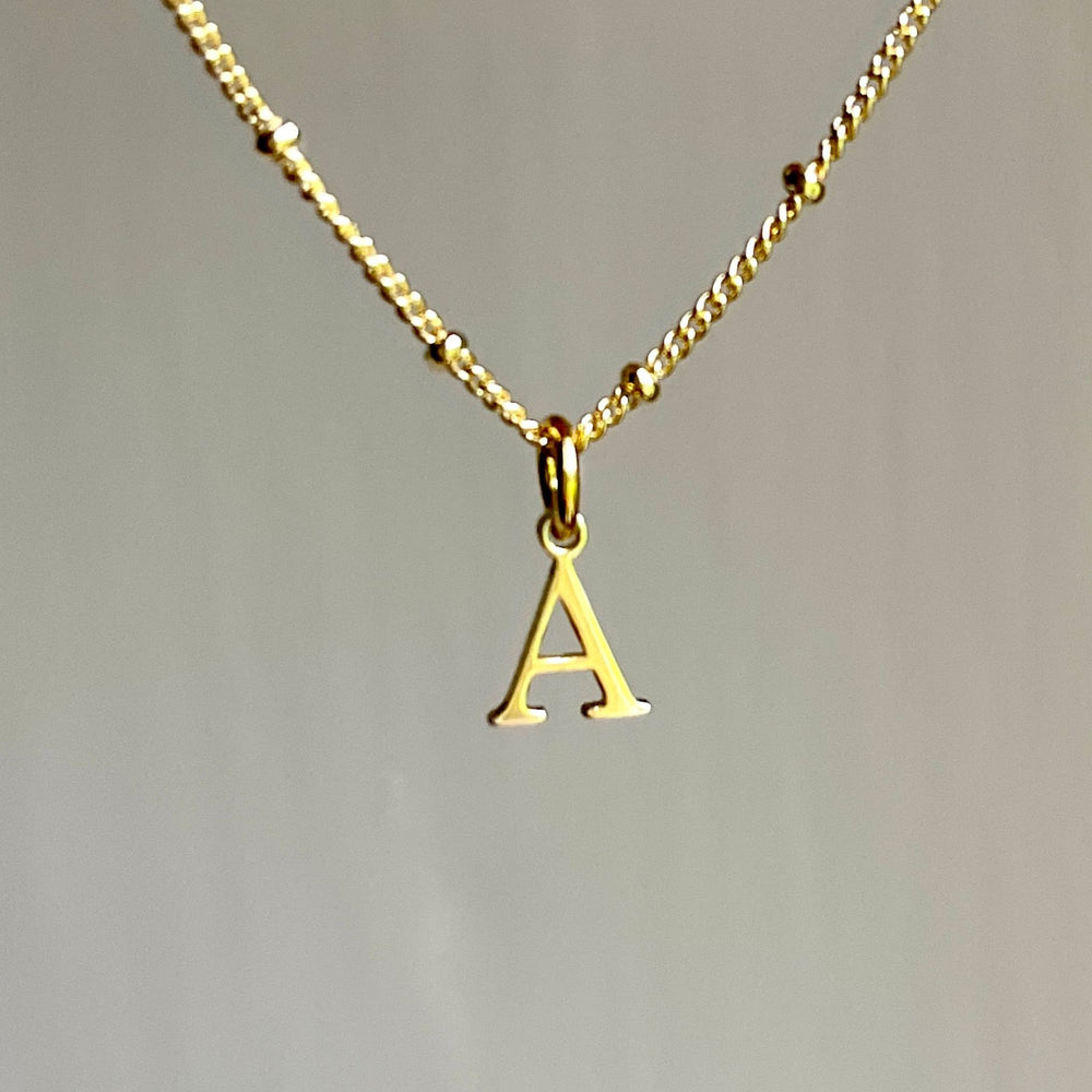 
                  
                    Gold initial necklace with an 'A' pendant on a plain background
                  
                