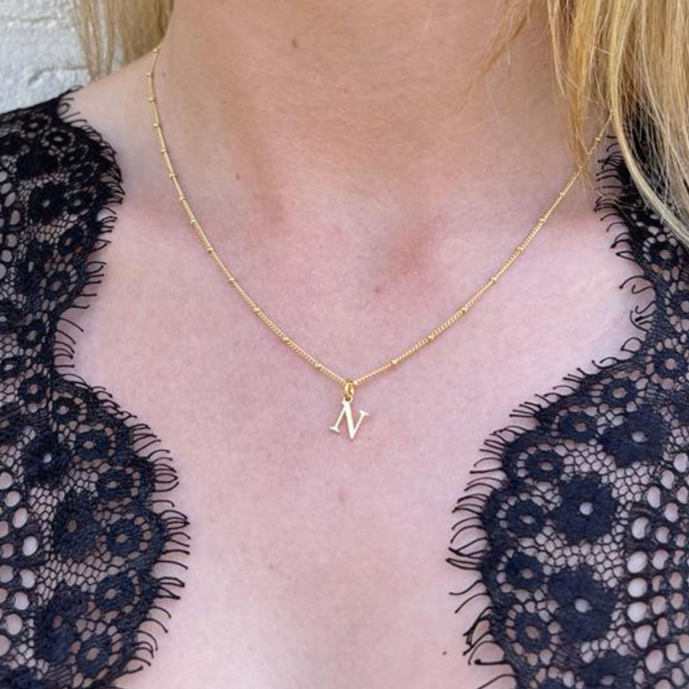 
                  
                    Gold initial necklace with a letter 'N' pendant worn by a model in a black lace top
                  
                