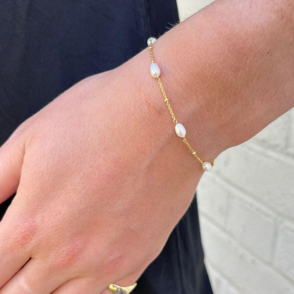 
                  
                    Model wears Helena pearl and gold bracelet against a neutral background
                  
                
