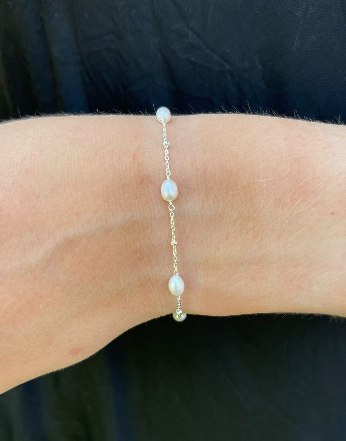 Helena pearl and silver bracelet on a wrist against a dark background