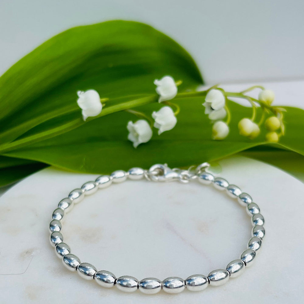 Jilly Sterling Silver Ball Bracelet on a tile with Lily of the Valley Flowers