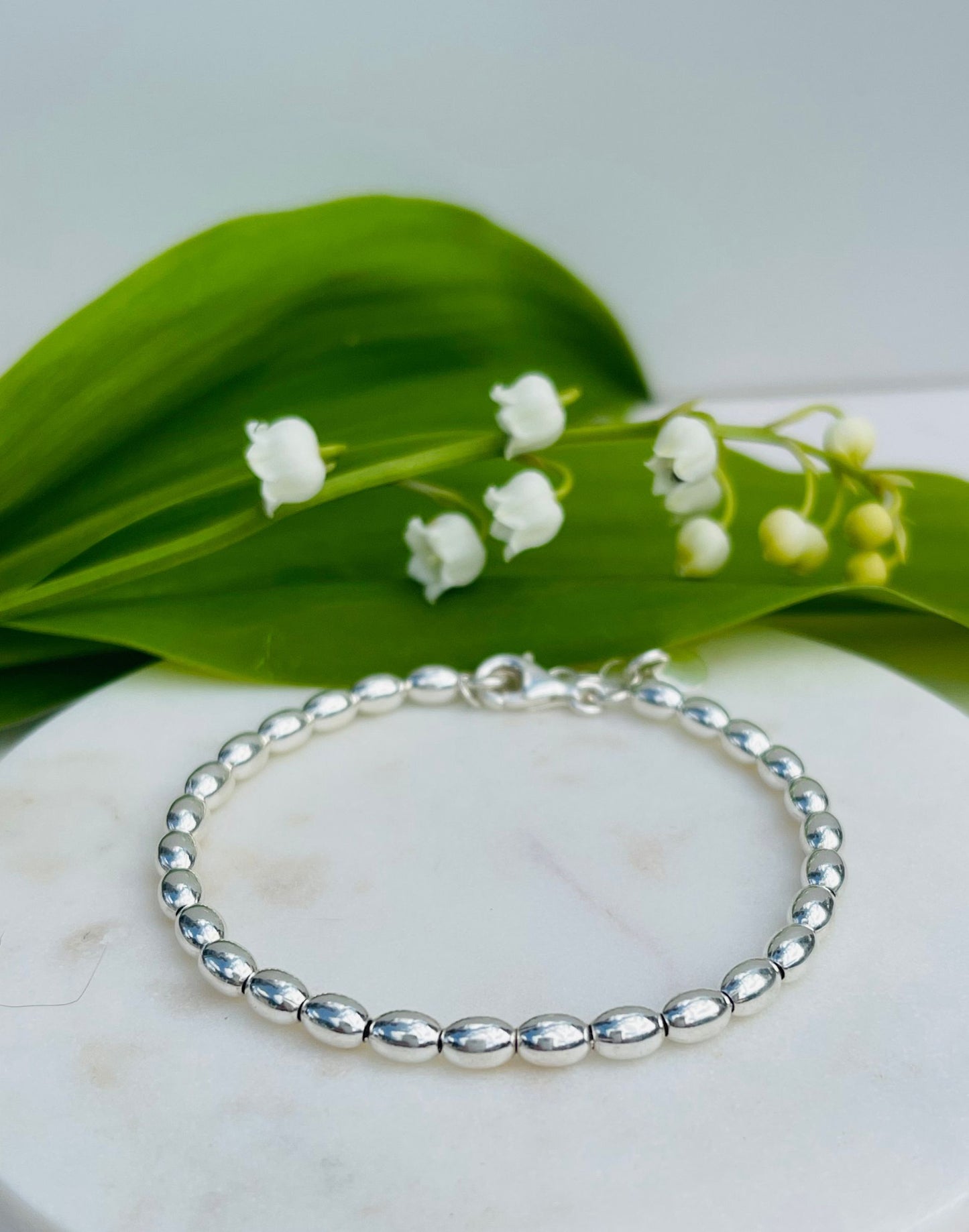 Jilly Sterling Silver Ball Bracelet on a tile with Lily of the Valley Flowers