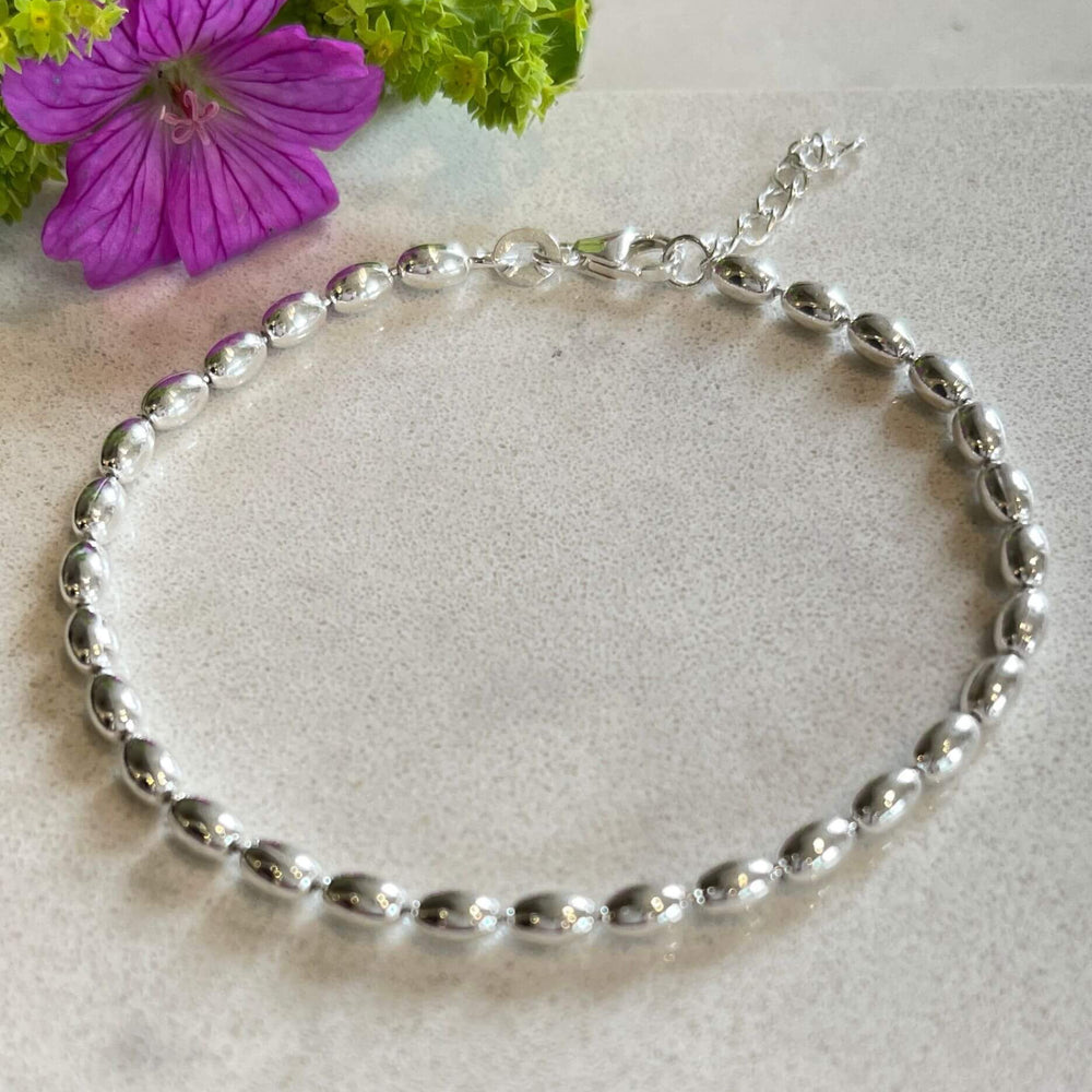 
                  
                    Jilly Sterling Silver Ball Bracelet on a light grey surface with a purple flower and green leaves.
                  
                