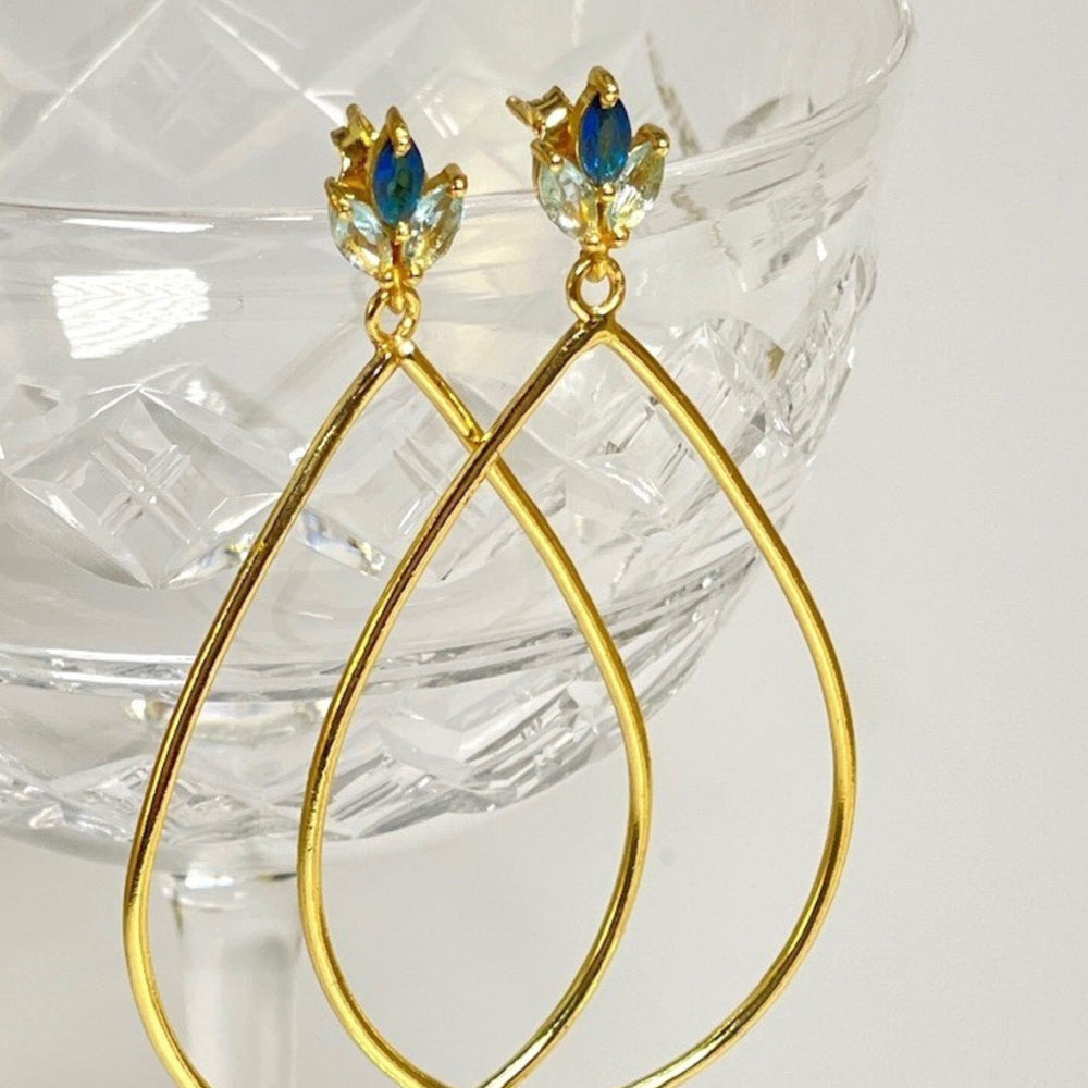 
                  
                    Lotus flower blue topaz gold earrings on glass
                  
                