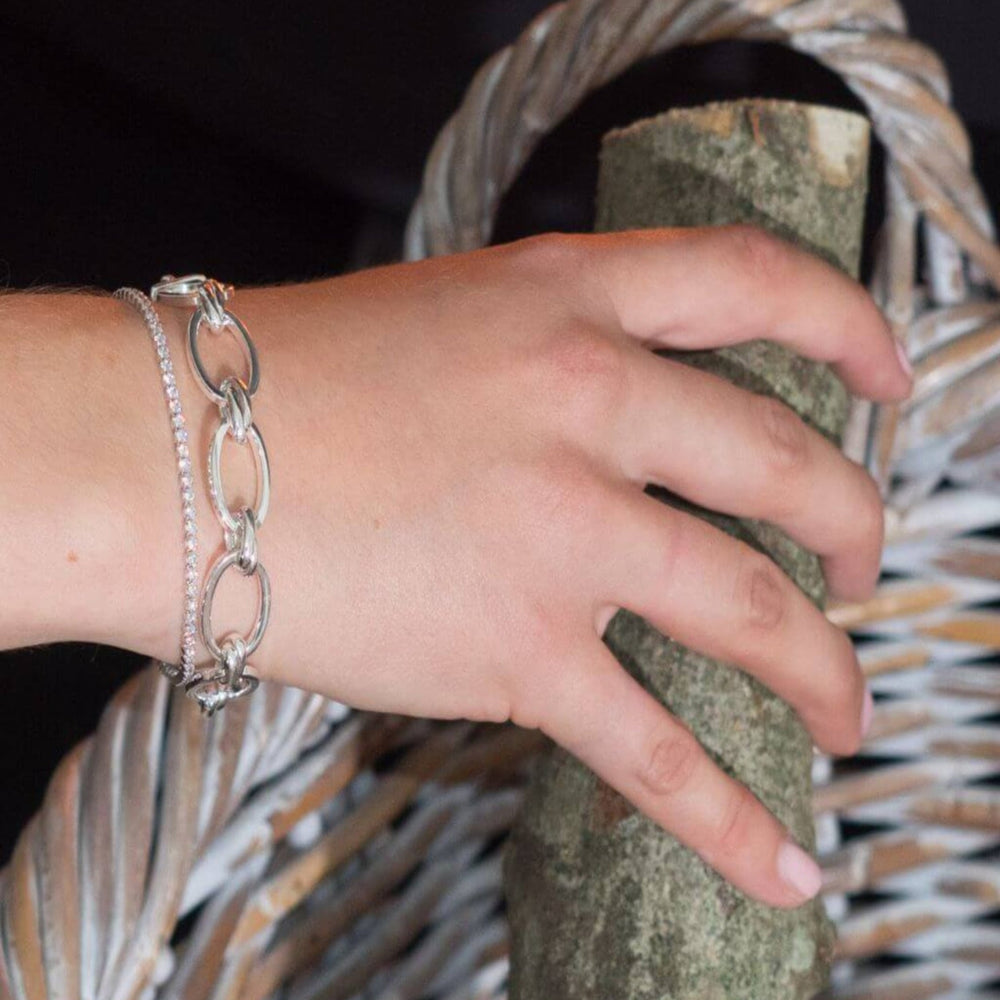 
                  
                    Hand wearing a lulu silver link bracelet holding a log 
against a woven basket background
                  
                