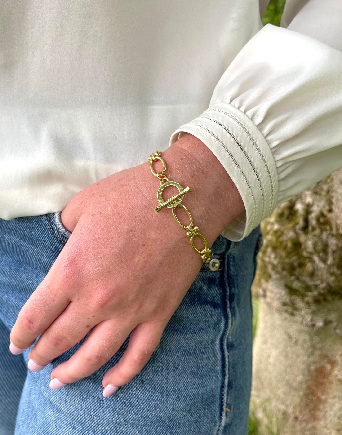 Jessica gold link bracelet on a wrist with a blurred natural background