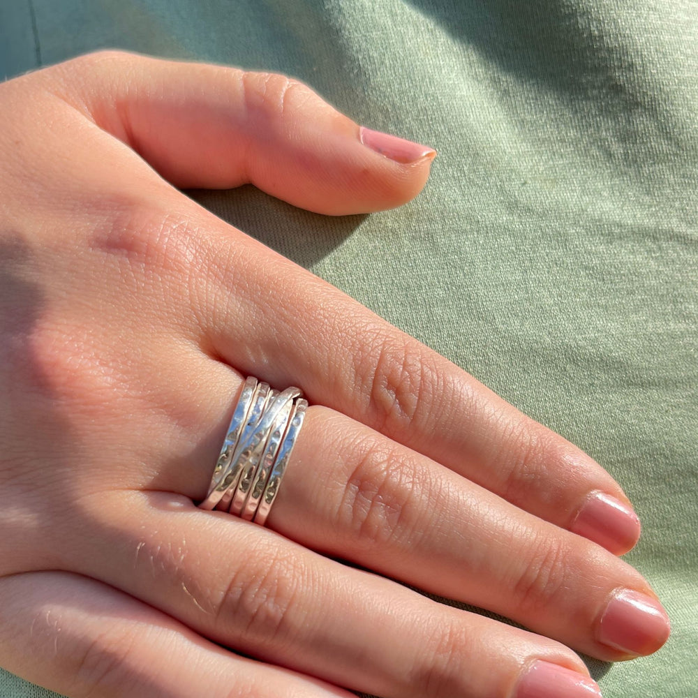 
                  
                    Model wearing multi band silver rings on a light green fabric background
                  
                