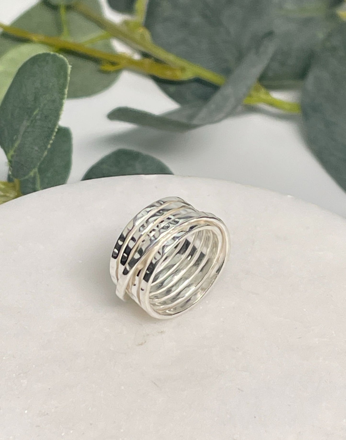 Multiband silver ring on a white surface with green leaves in the background