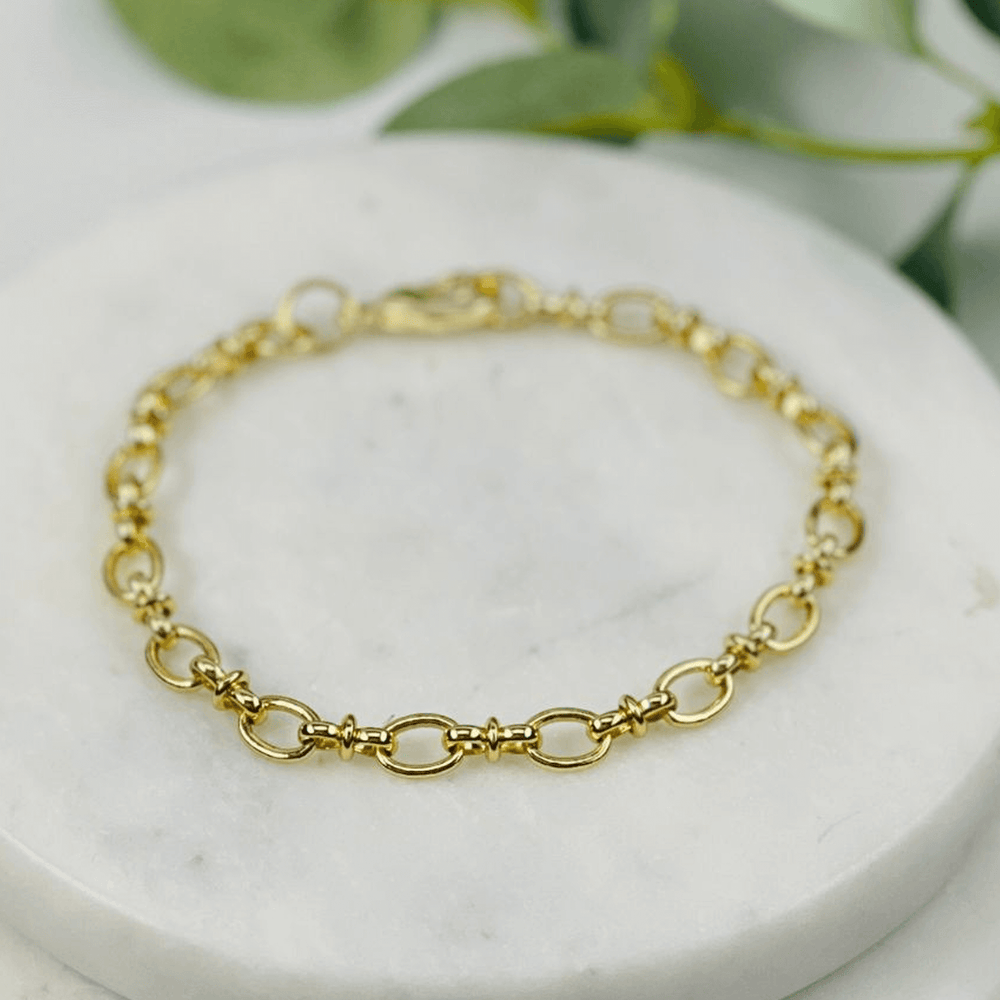 Pippa Link Gold bracelet on a marble surface with green leaves in the background
