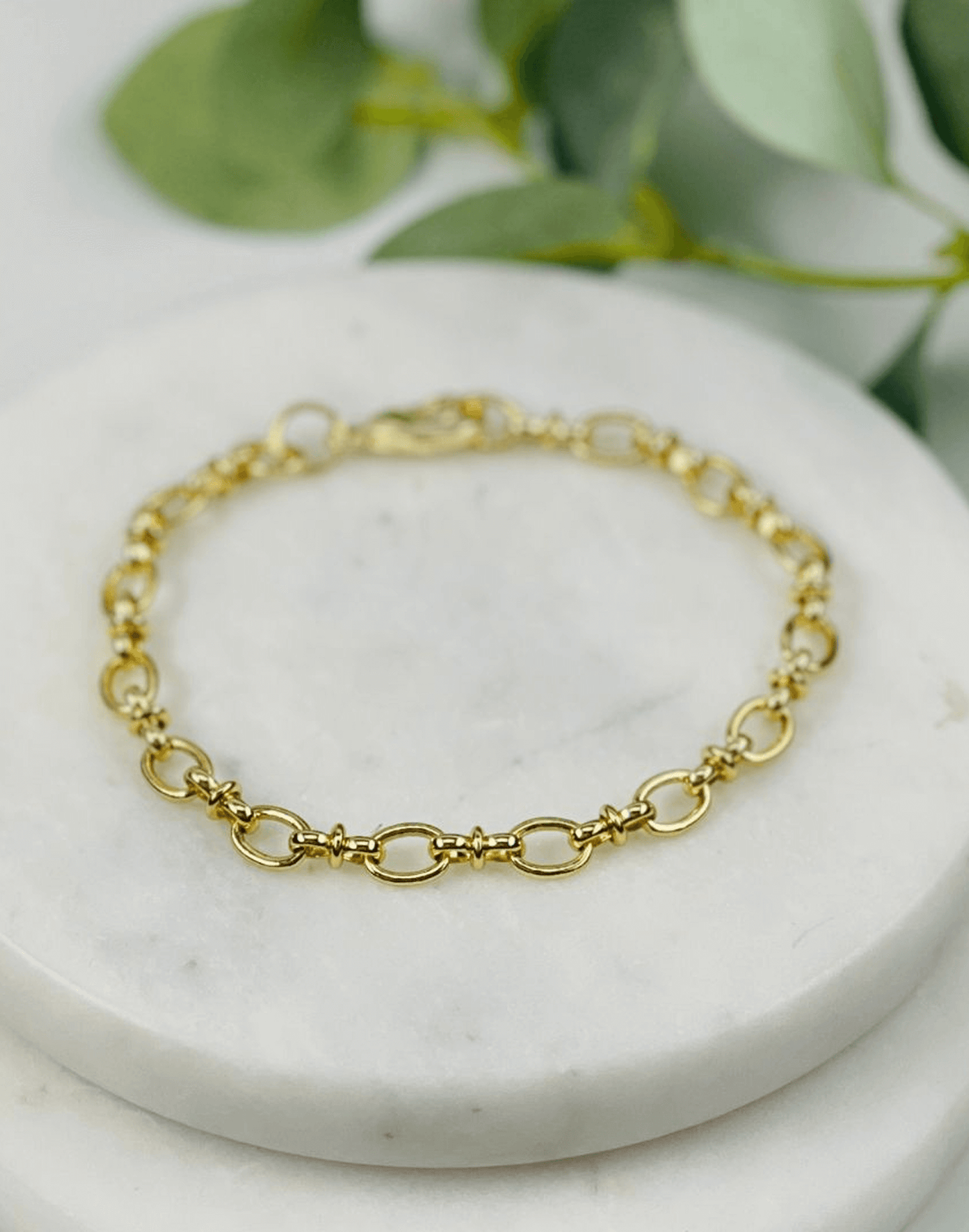 Pippa Link Gold bracelet on a marble surface with green leaves in the background