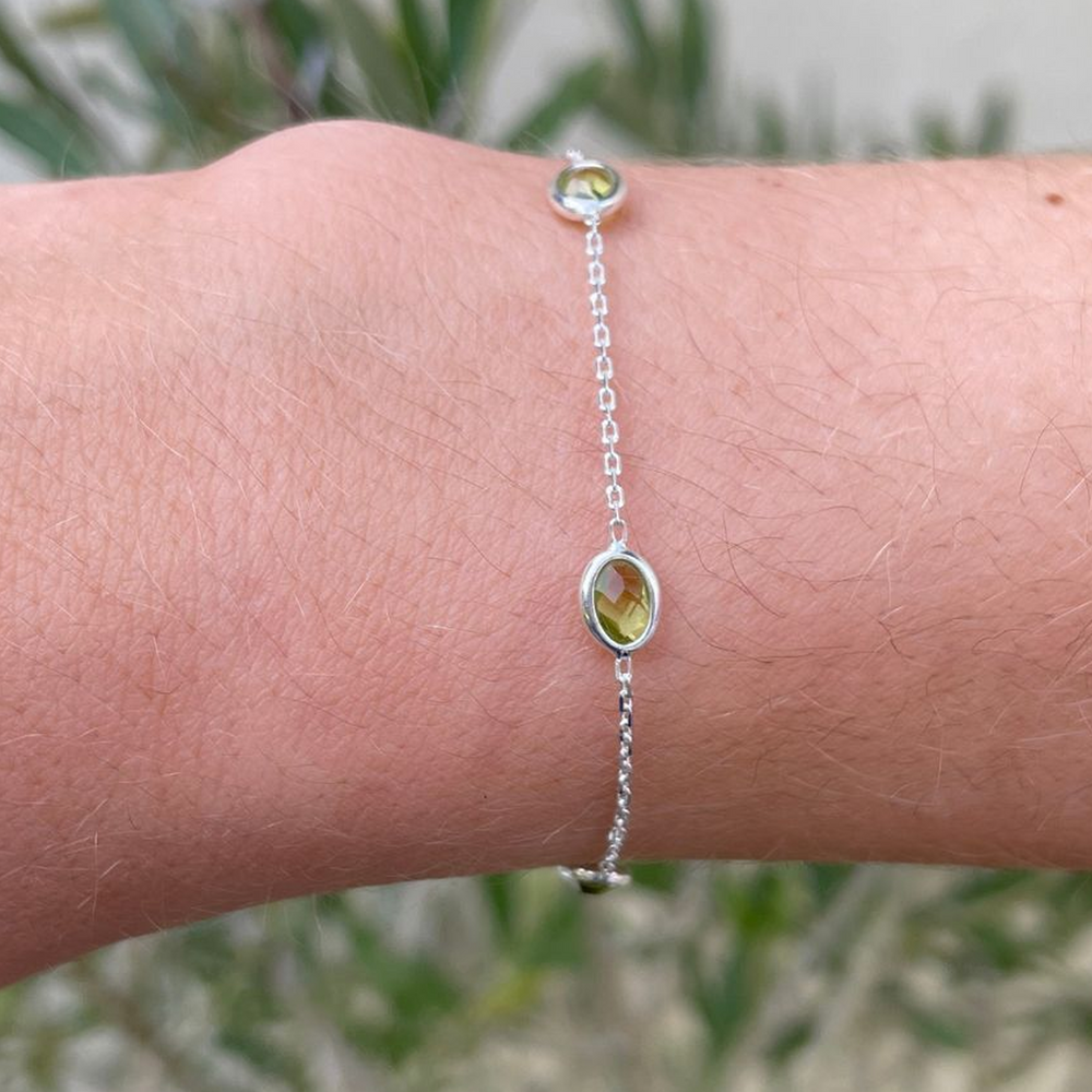 Silver bracelet with green lab grown peridot on a wrist against a blurred natural background