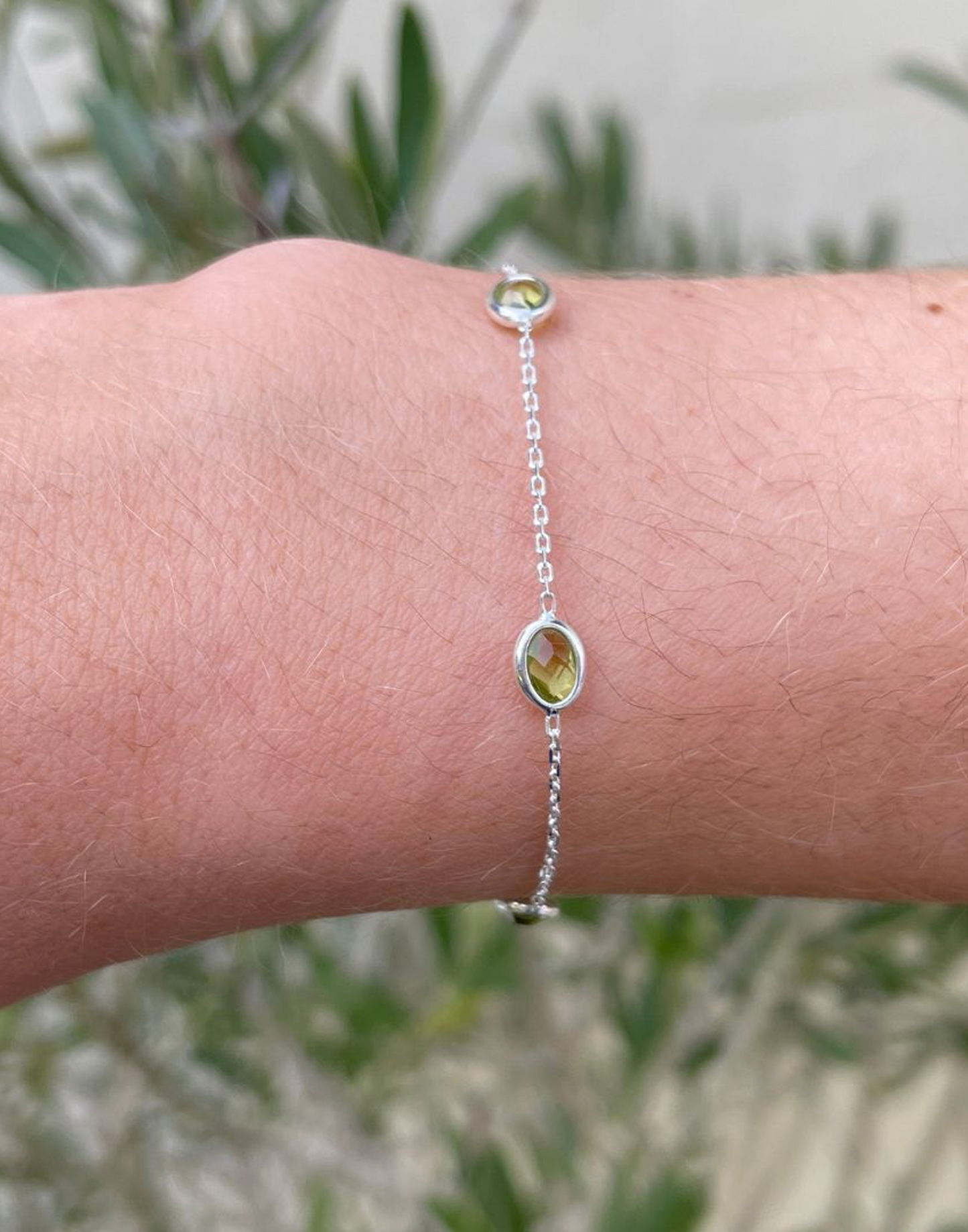 Silver bracelet with green lab grown peridot on a wrist against a blurred natural background