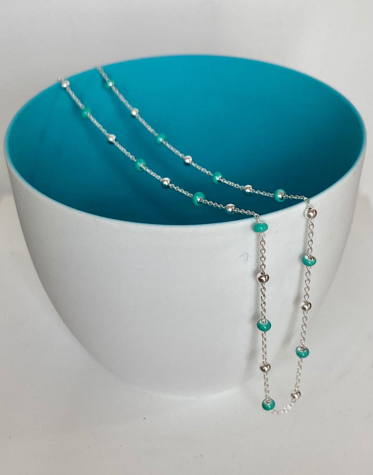 Silver light turquoise enamel necklace draped over a bowl