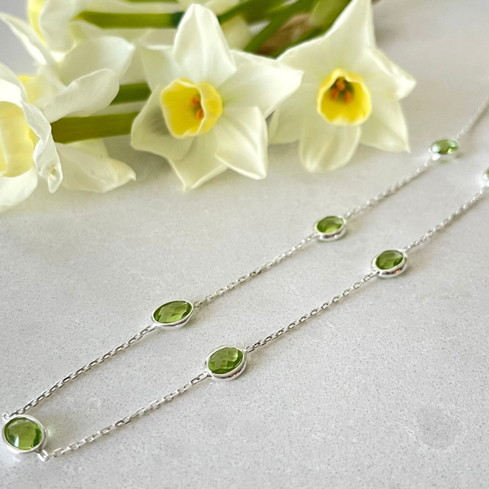 
                  
                    Silver Peridot Necklace lying on stone surface
                  
                