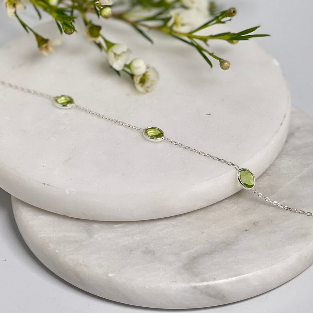 Silver bracelet with lab grown peridot stones on a marble surface with flowers