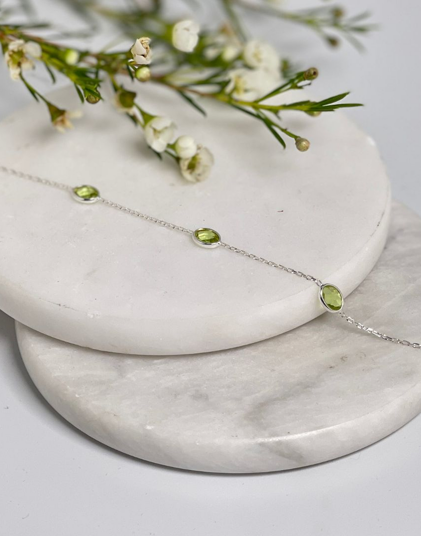 Silver bracelet with lab grown peridot stones on a marble surface with flowers
