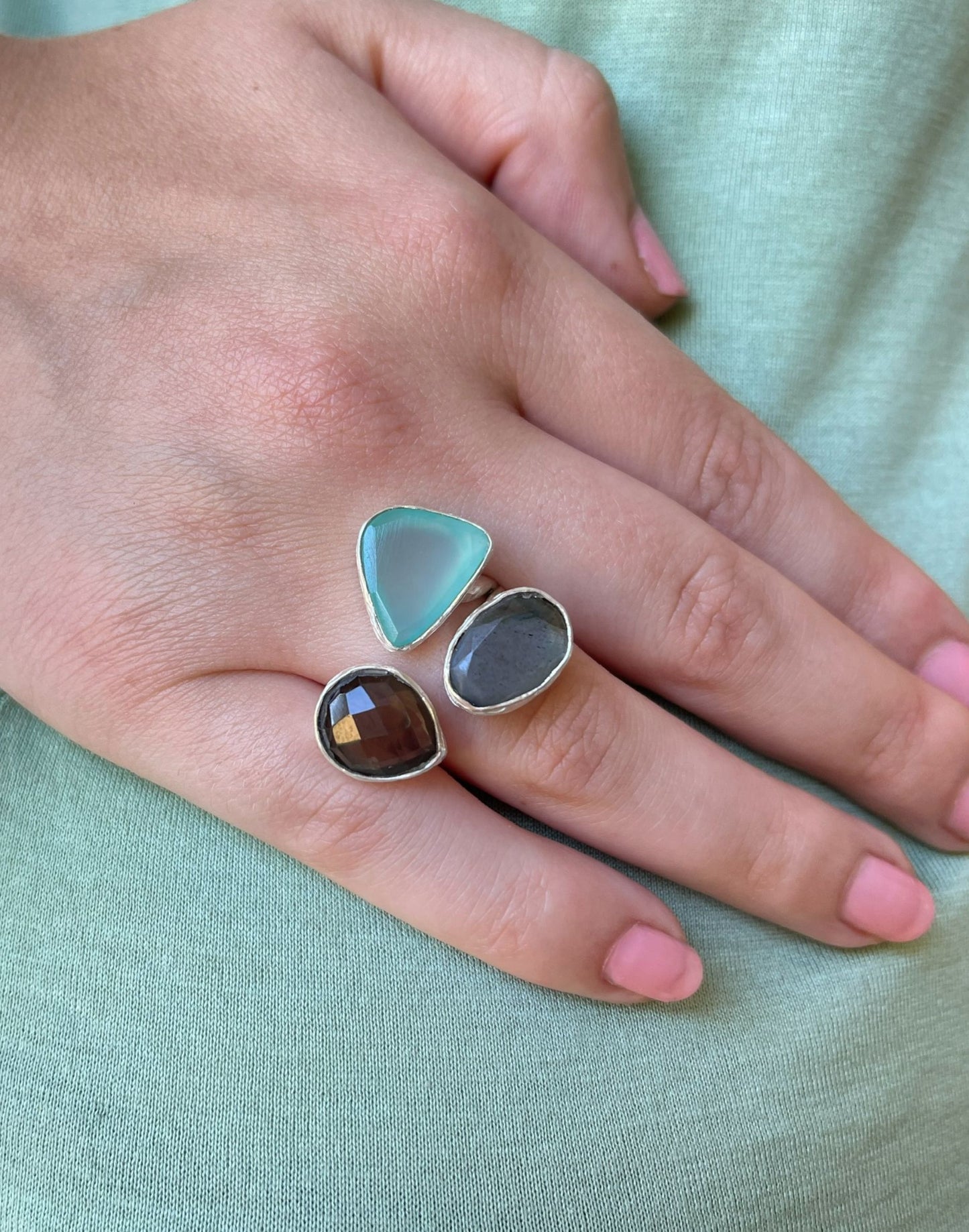 model wears a pretty stone and silver chunky ring on a light green fabric background