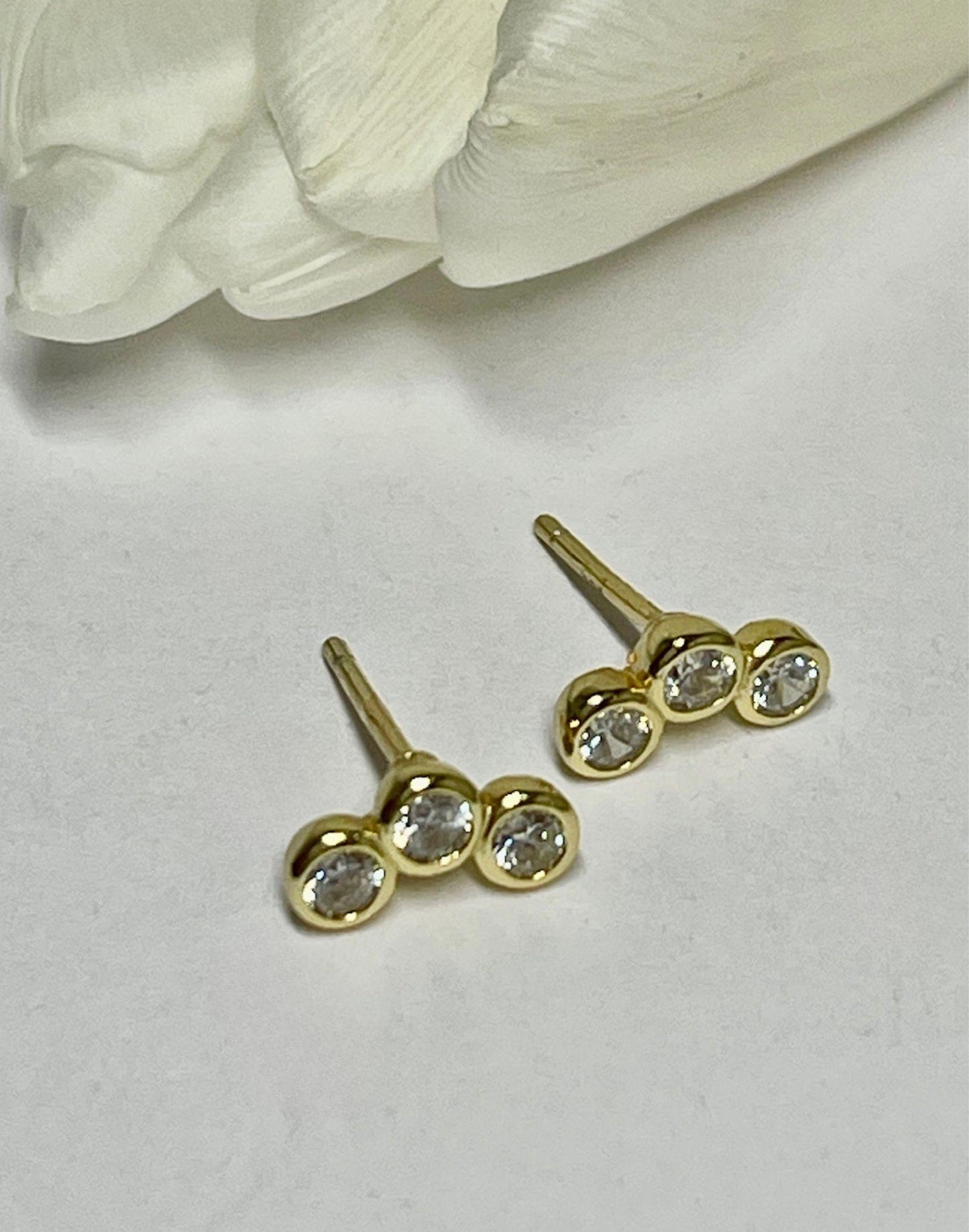 Triple Cubic Zirconia Gold stud earrings lying by a tulip
