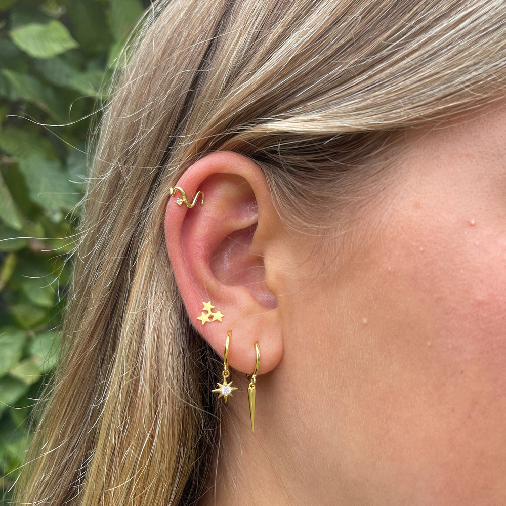 Close-up of a person wearing gold earrings with a blurred green background