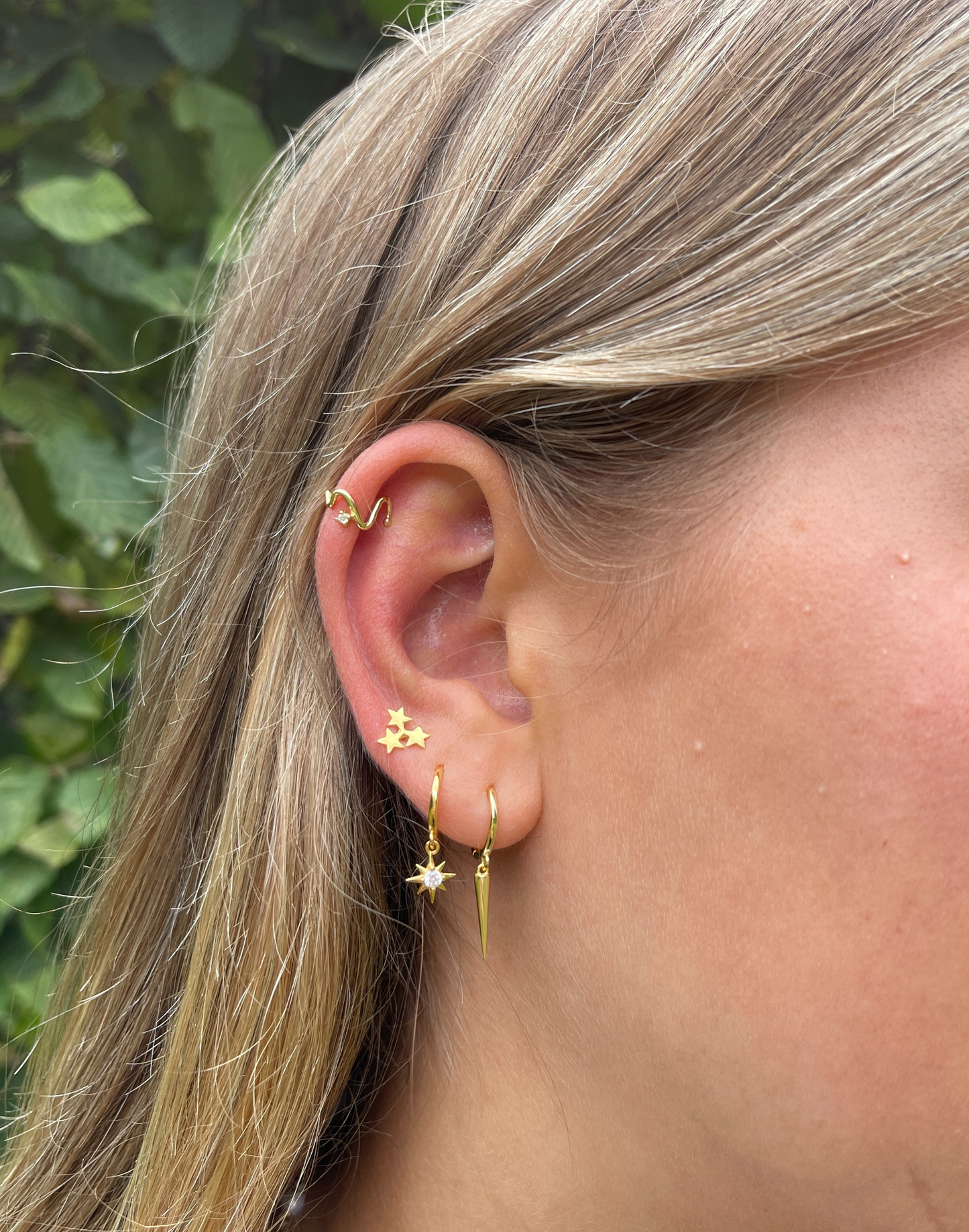 Close-up of a person wearing gold earrings with a blurred green background