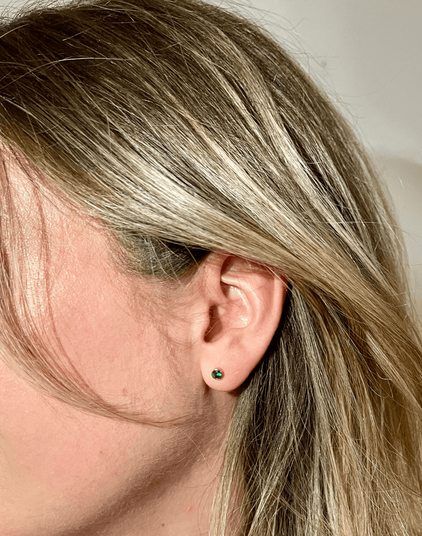 green coloured birthstone studs in model's ear