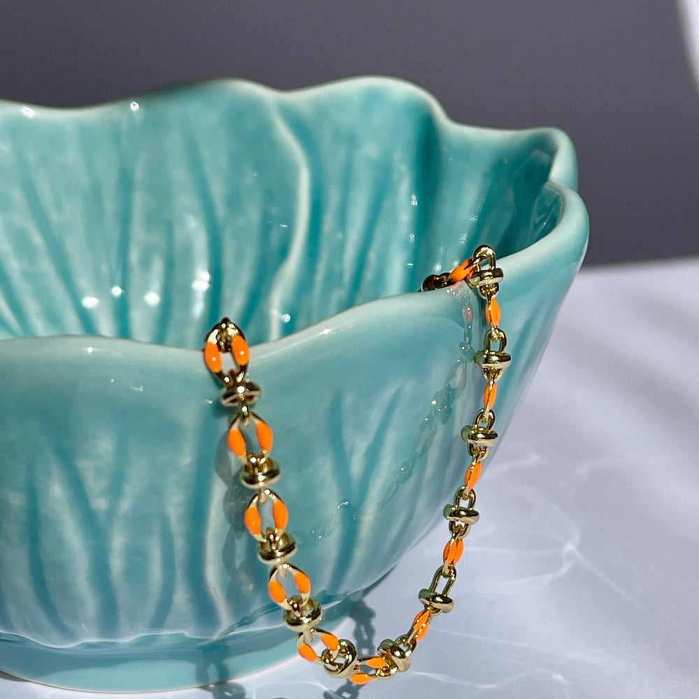 
                  
                    Orange enamel bracelet draped over a teal coloured bowl
                  
                