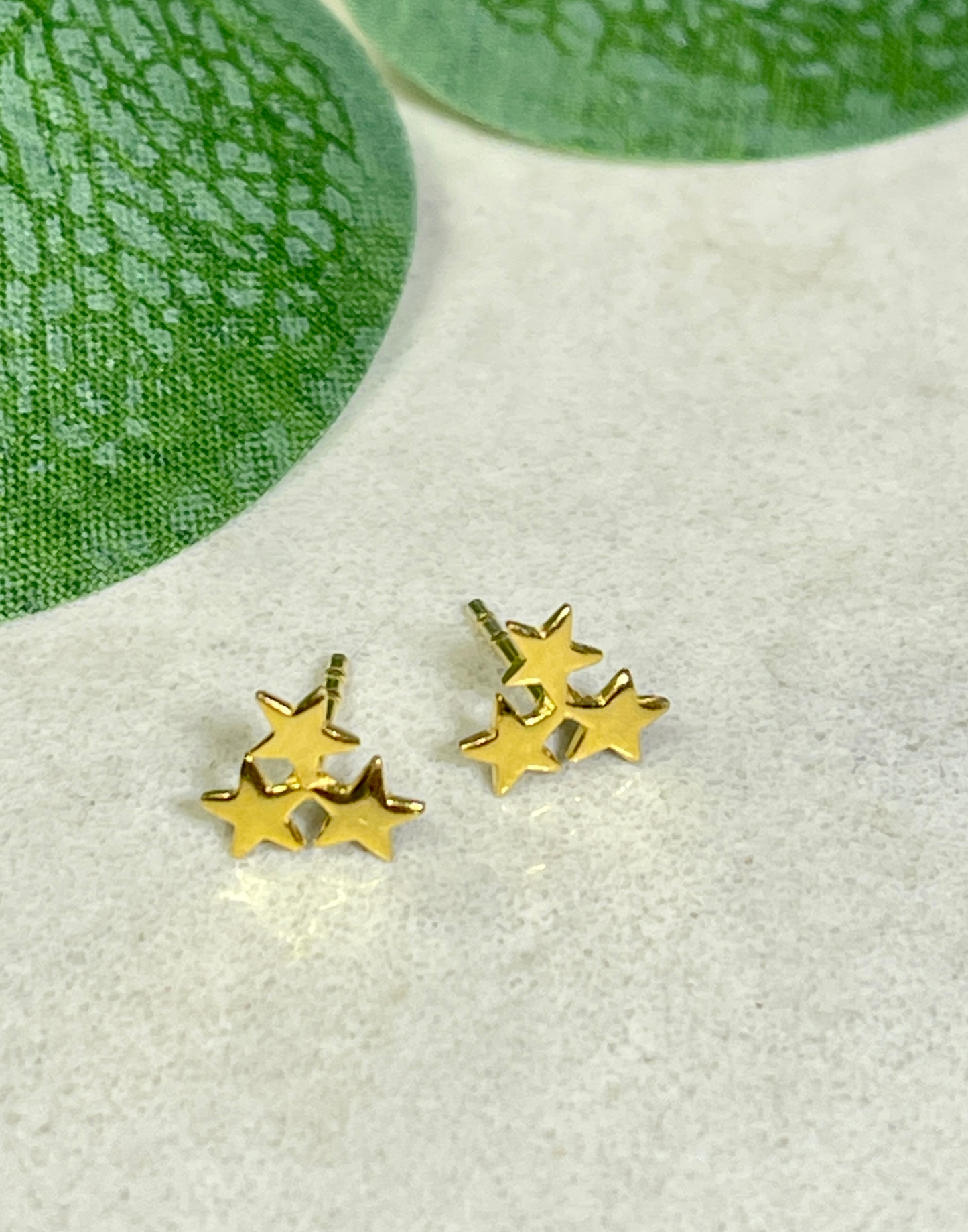 Gold star-shaped earrings on a light gray surface with green leaves in the background